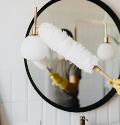 Limpieza Abella Orteguerira Coruña A person cleaning an elegant bathroom mirror with a fluffy duster and yellow gloves.